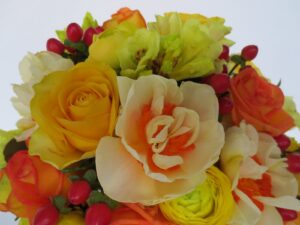 a bouquet of yellow orange and red flowers including yellow roses yellow ranunculi orange roses yellow rhododendron red hypericum berry and yellow daffodils